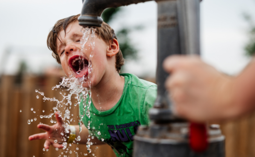 little boy with mouth open over water pump